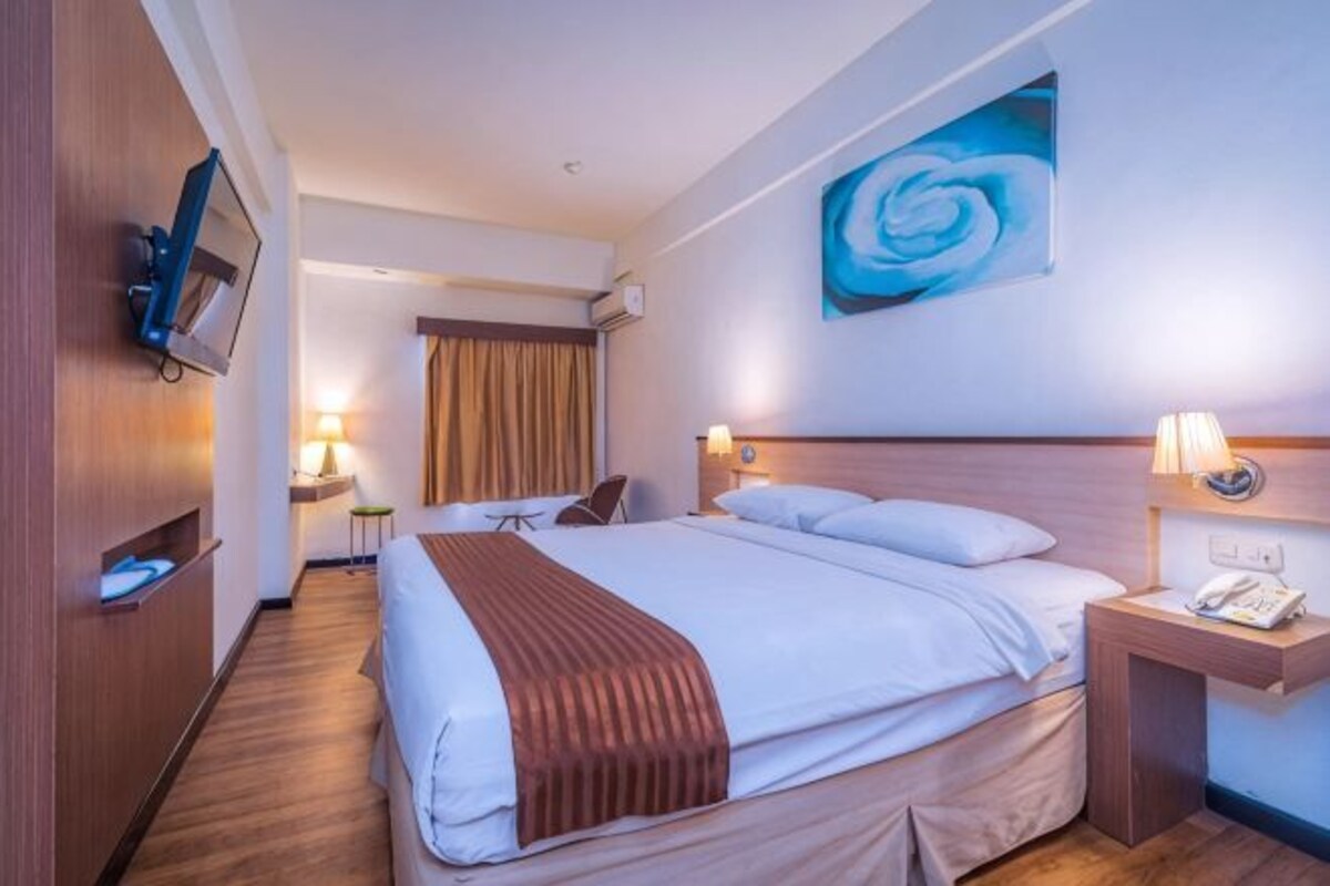 A hotel room with a large bed, bedside tables, a TV, and a painting on the wall.