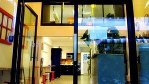 A modern building with a glass entrance, a visible kitchen area, and a dining space with tables and chairs. - de Talak (Bangkok)