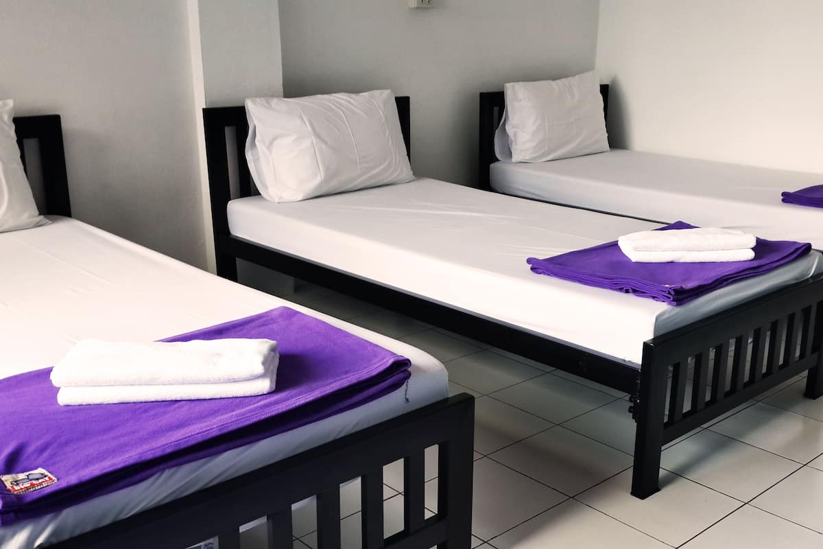 Three single beds with white linens and purple towels, arranged in a row with black headboards.