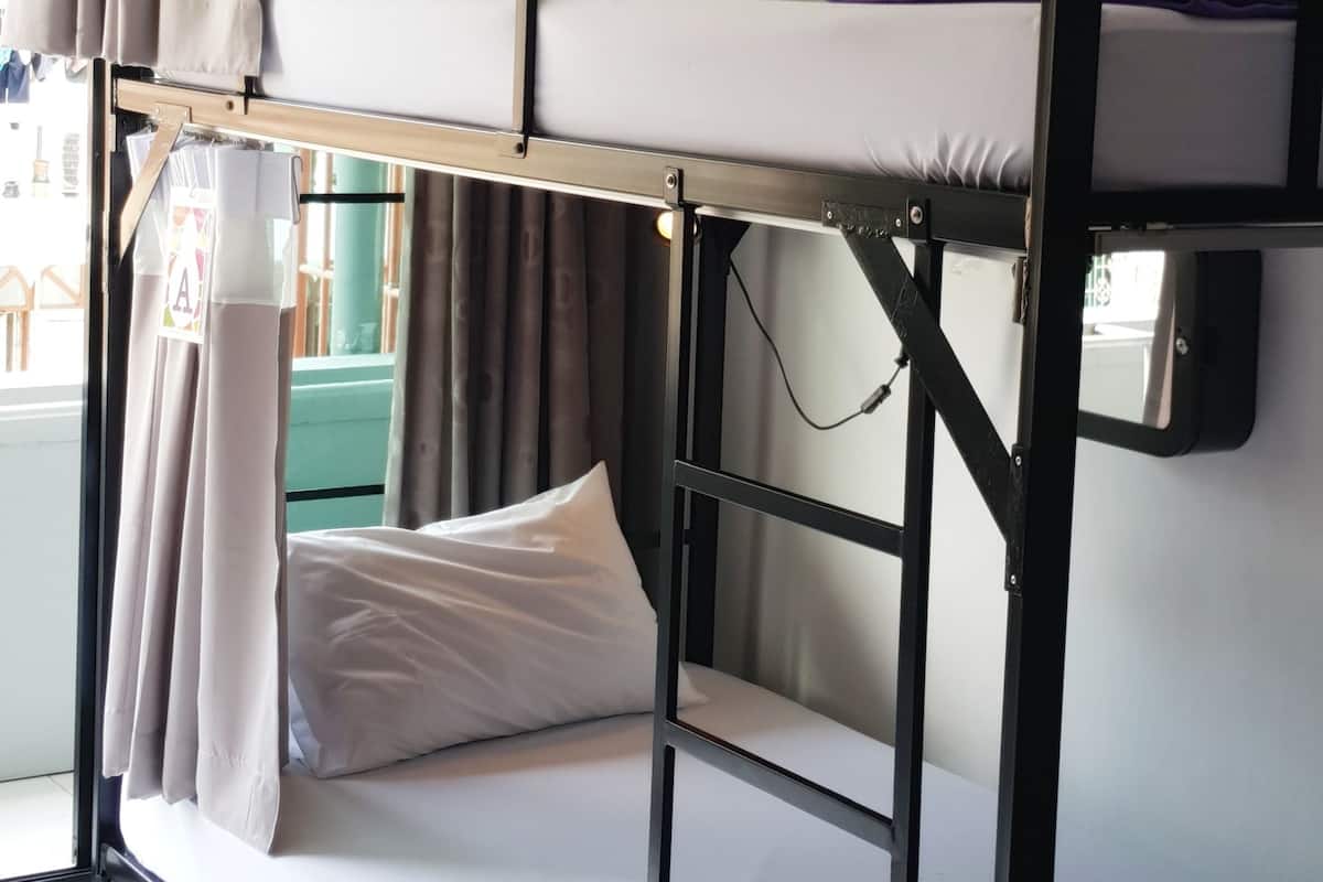 A bunk bed room with a window, curtains, and a bedside lamp.