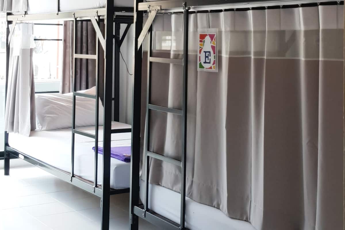 A dormitory-style room with bunk beds, each with a curtain and a small sign.