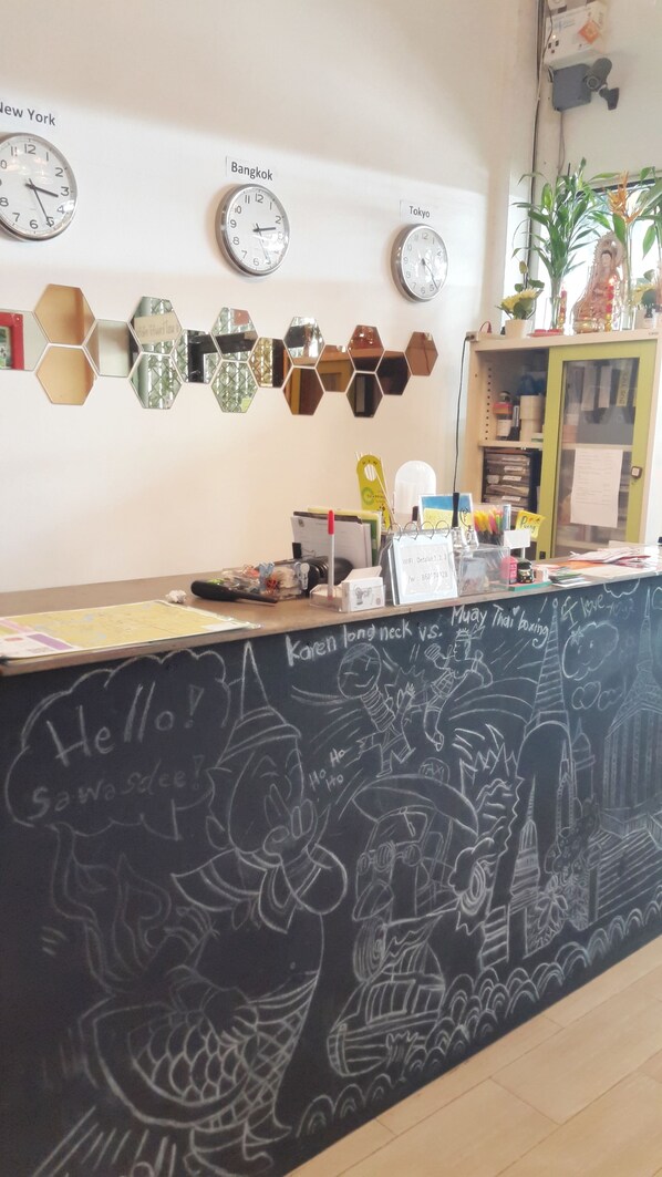 Una recepción con relojes que marcan la hora en Nueva York, Bangkok y Tokio, una pizarra con dibujos y notas, y una planta a la derecha.