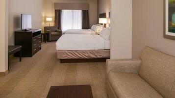 A hotel room with a bed, a sofa, a desk with a television, and a chair.