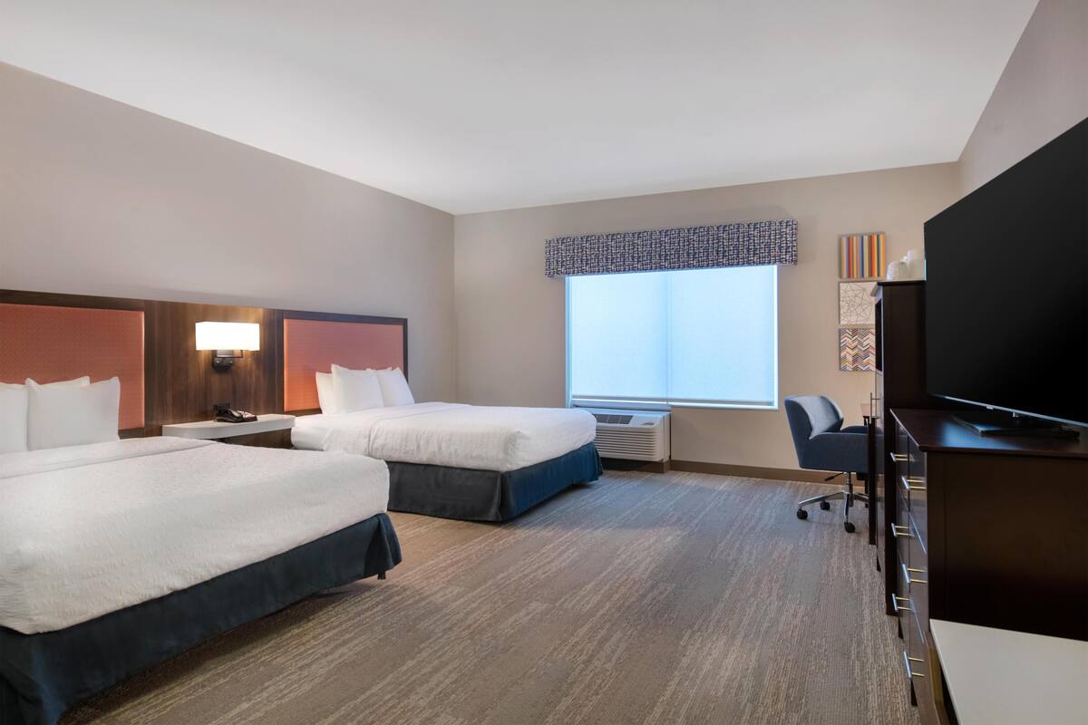 Une chambre d’hôtel avec deux lits, un bureau, une chaise, une télévision et une fenêtre donnant sur un beau paysage.