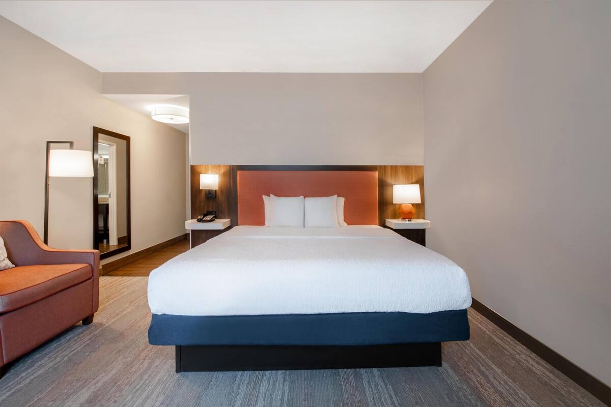 Une chambre d’hôtel avec un grand lit, une chaise, une table de chevet avec une lampe et un miroir.