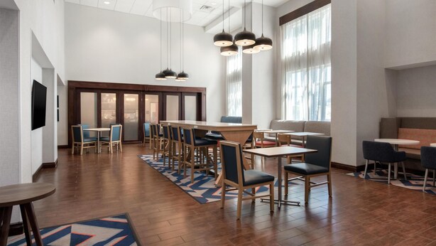 A spacious hotel lobby with a central bar, multiple seating areas, and large windows allowing natural light.
