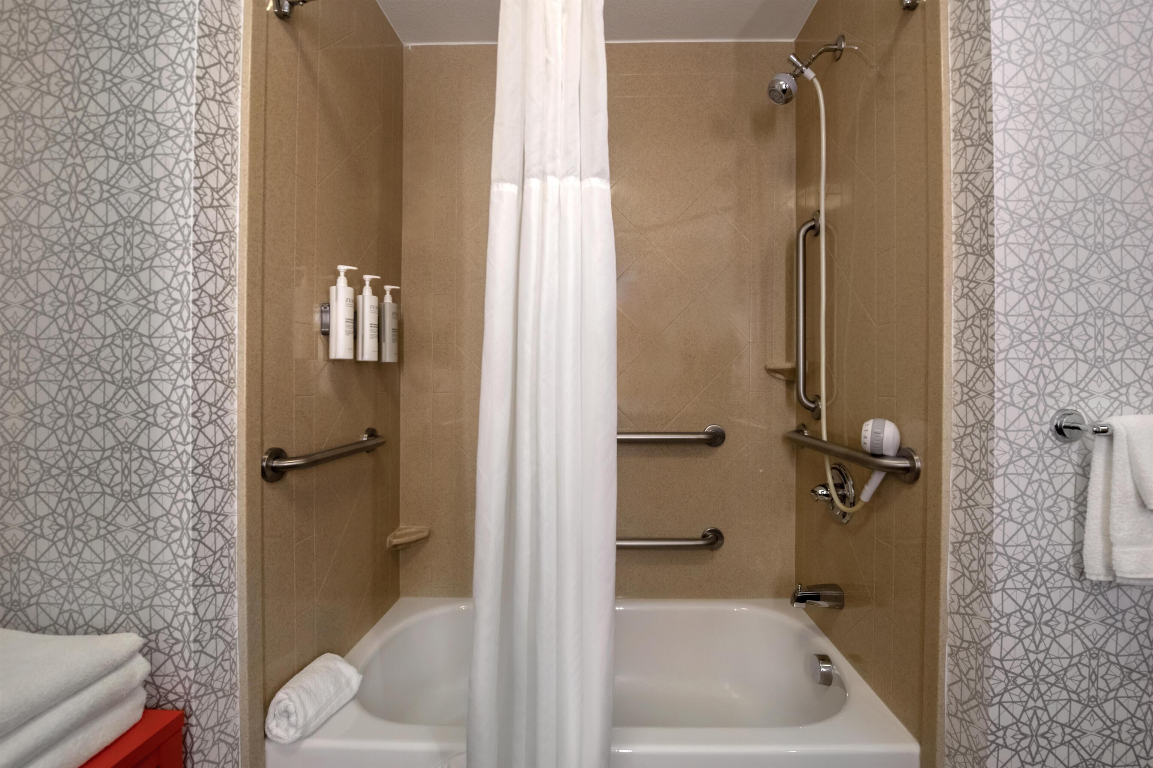 A bathroom with a bathtub, shower, and handrails.
