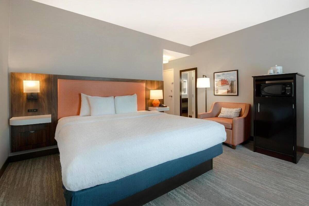 Une chambre d’hôtel avec un grand lit, des tables de chevet, une chaise, une armoire et un four à micro-ondes.