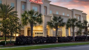 A Hampton Inn & Suites hotel with a modern facade, palm trees, and a well-lit entrance.