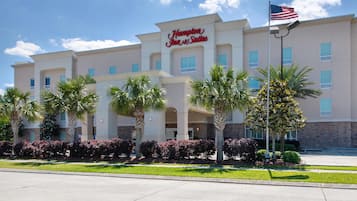A Hampton Inn & Suites hotel with a modern facade, palm trees, and a clear sky.