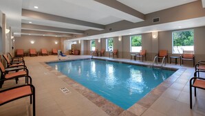An indoor swimming pool with multiple lanes, surrounded by chairs and tables, and large windows providing natural light.