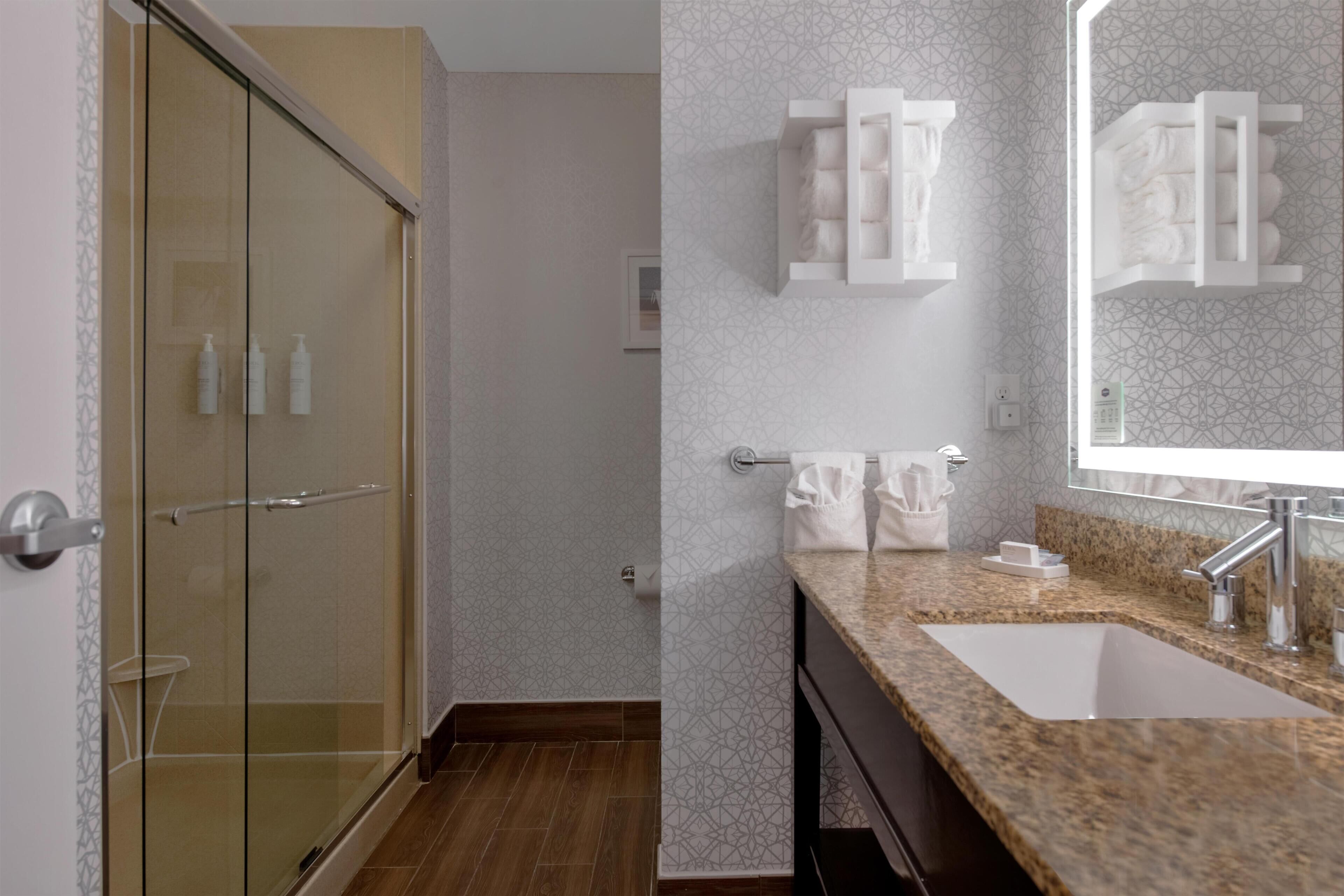 Un baño moderno con cabina de ducha de vidrio, lavamanos de granito y toallero de pared.