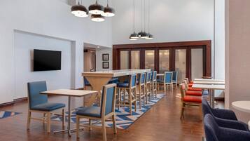 Un hall d’hôtel moderne doté d’un long comptoir, de plusieurs espaces salon et d’un téléviseur à écran plat fixé au mur.