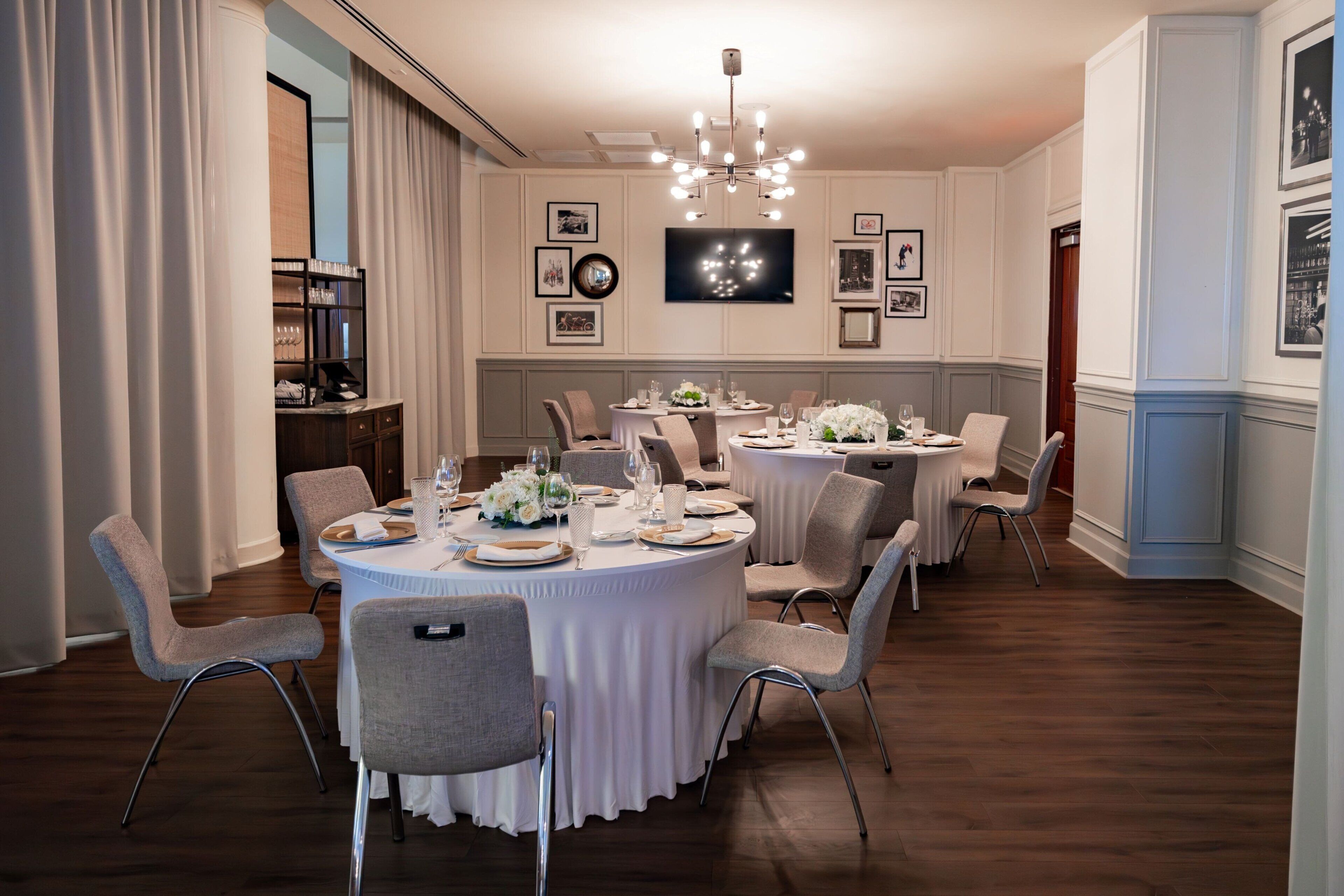 A formal dining room with round tables, white tablecloths, and grey chairs.