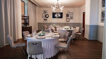 A formal dining room with round tables, white tablecloths, and grey chairs.