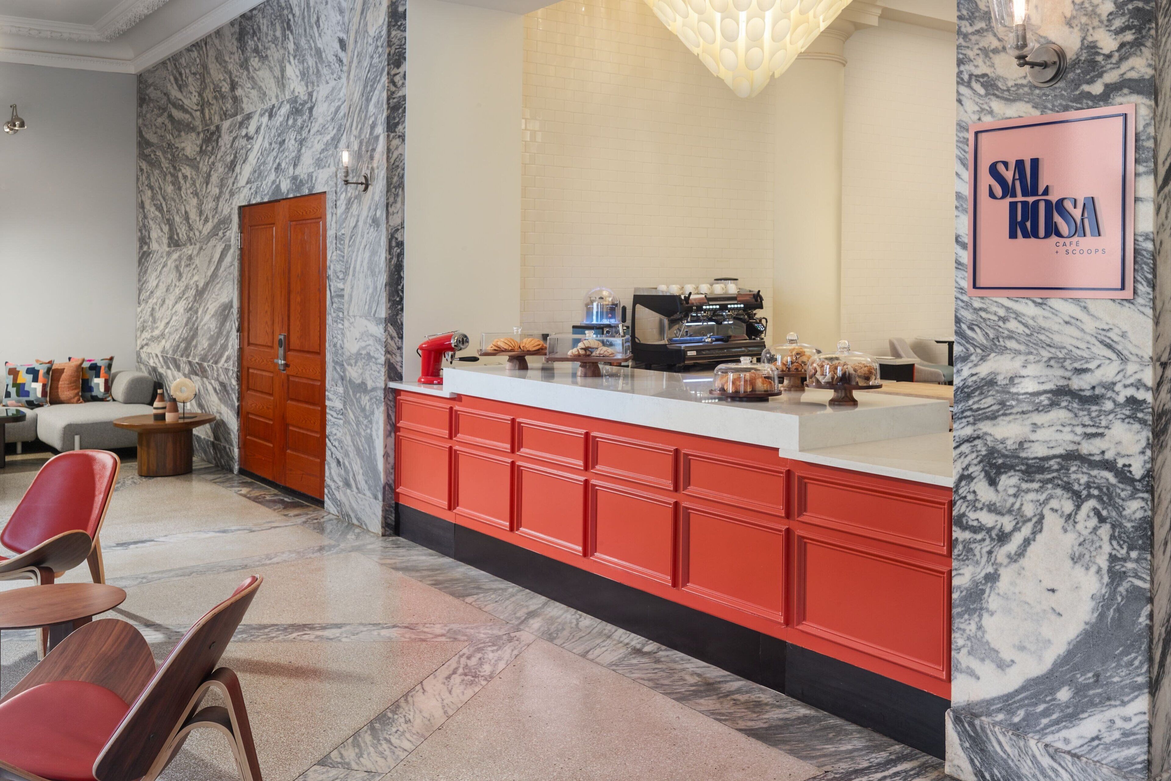 Um café moderno com paredes de mármore, um balcão vermelho e uma placa com a inscrição 'SAL ROSA CAFE & SCOOPS'.