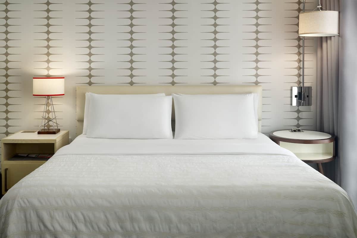 A hotel room with a large bed, two bedside tables, a lamp, a mirror, and a wall with a geometric pattern.
