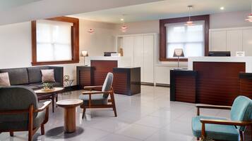 A modern hotel lobby with a reception desk, seating area with sofas and chairs, and large windows providing natural light.