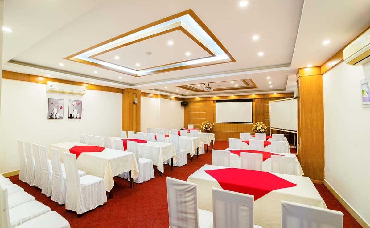 Un salón de conferencias con varias mesas y sillas, equipado con una pantalla de proyector y unidades de aire acondicionado.