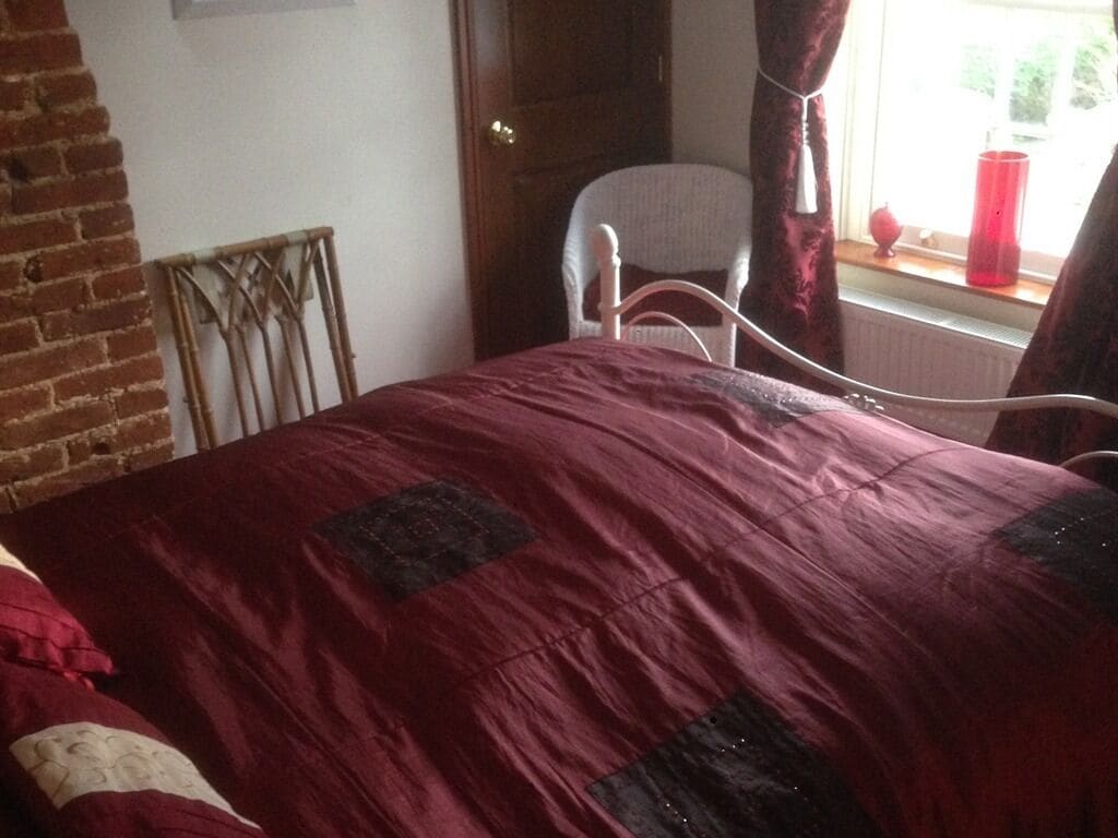 Un dormitorio con cama, una silla, una ventana con cortinas y una pared de ladrillo.