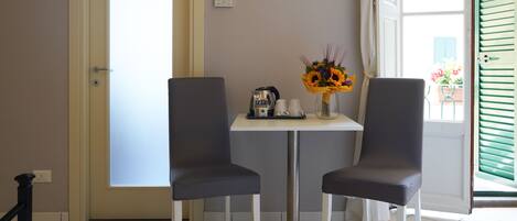 A room with two chairs, a table, a coffee maker, and a vase with flowers.