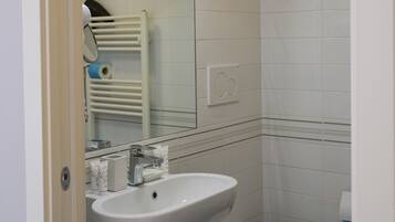 Un baño con lavamanos blanco, inodoro, espejo y perchero para toallas.