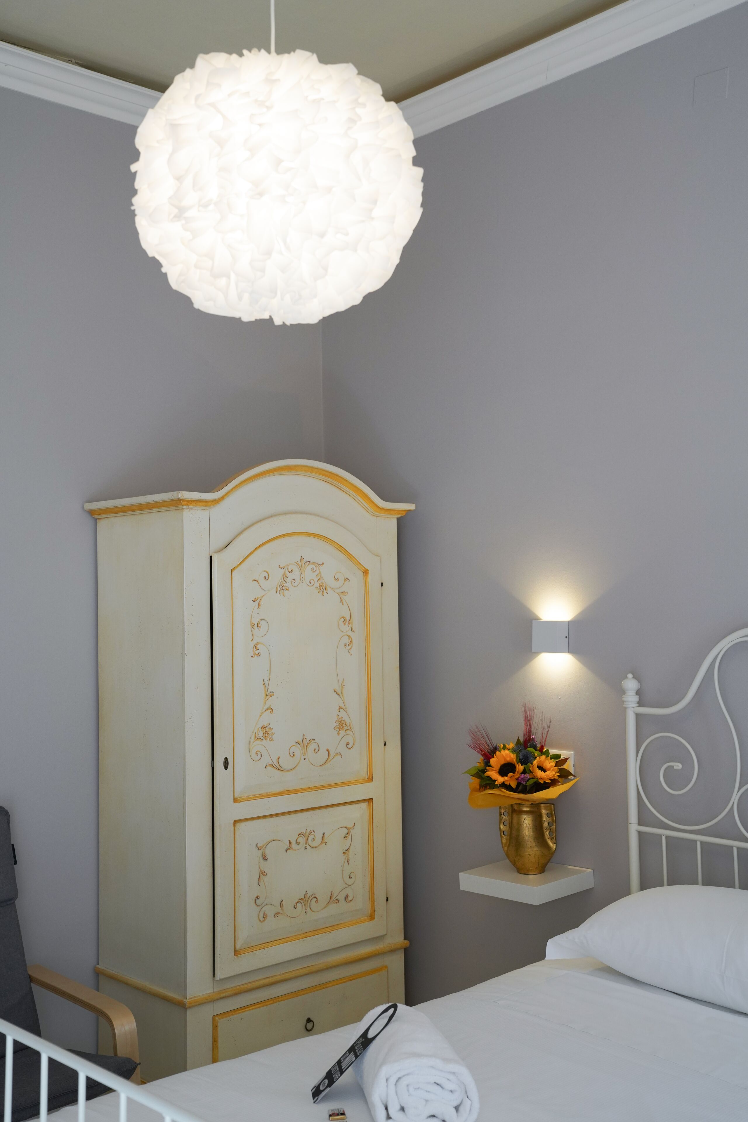 Ein Schlafzimmer mit einem weißen Bett, einem weißen Kleiderschrank, einer Pendelleuchte und einer Wandleuchte.