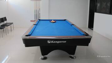 Een pooltafel met een blauwe viltkleed, een Kangaroo logo, en een biljarthouder met biljartkeus. Er staan stoelen en een ingelijst beeld op de muur.