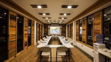 A conference room with a long table, chairs, a projector screen, and wooden panel walls.