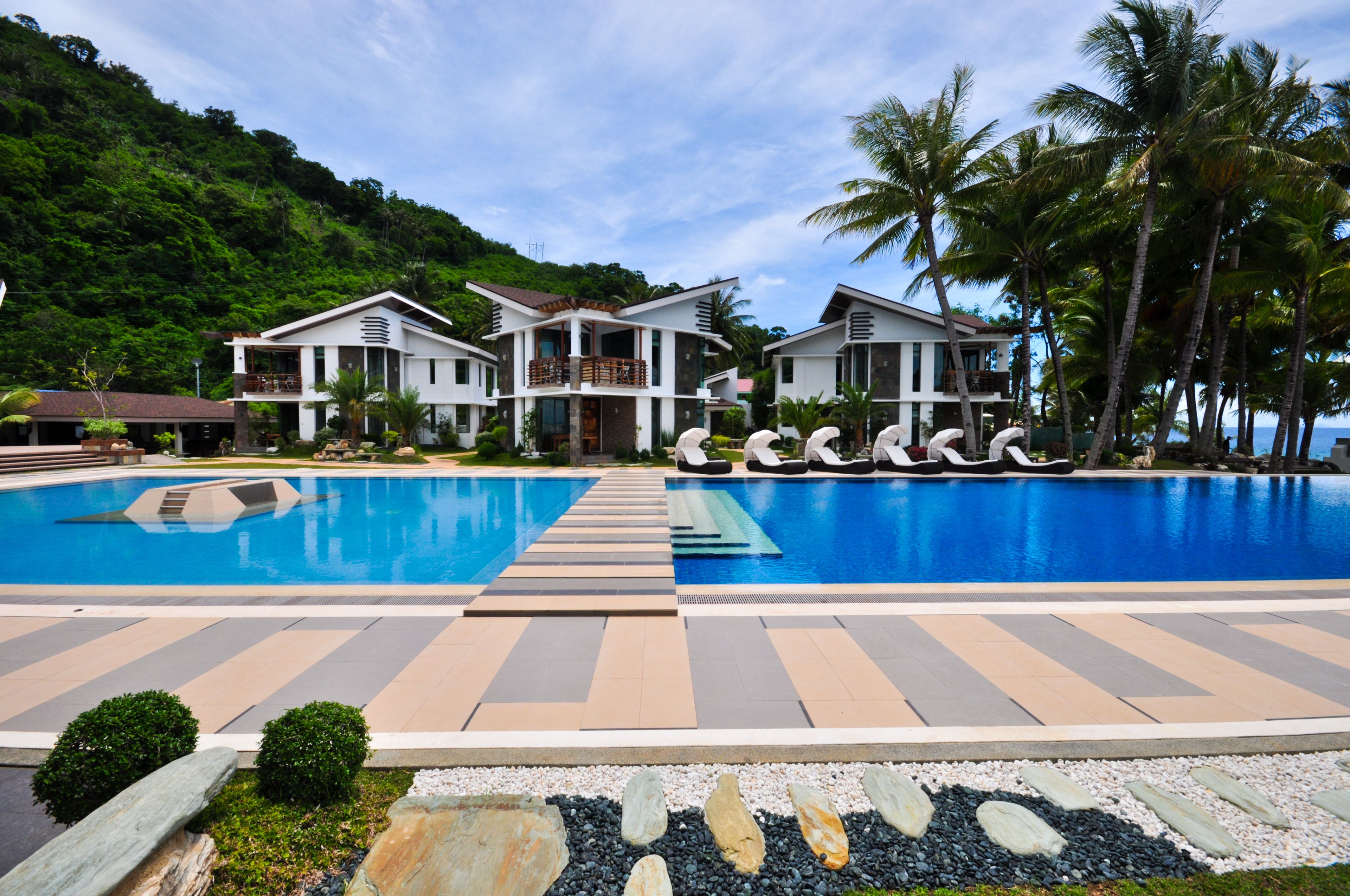 Un resort con una gran piscina, varias villas para huéspedes y un paisaje tropical.