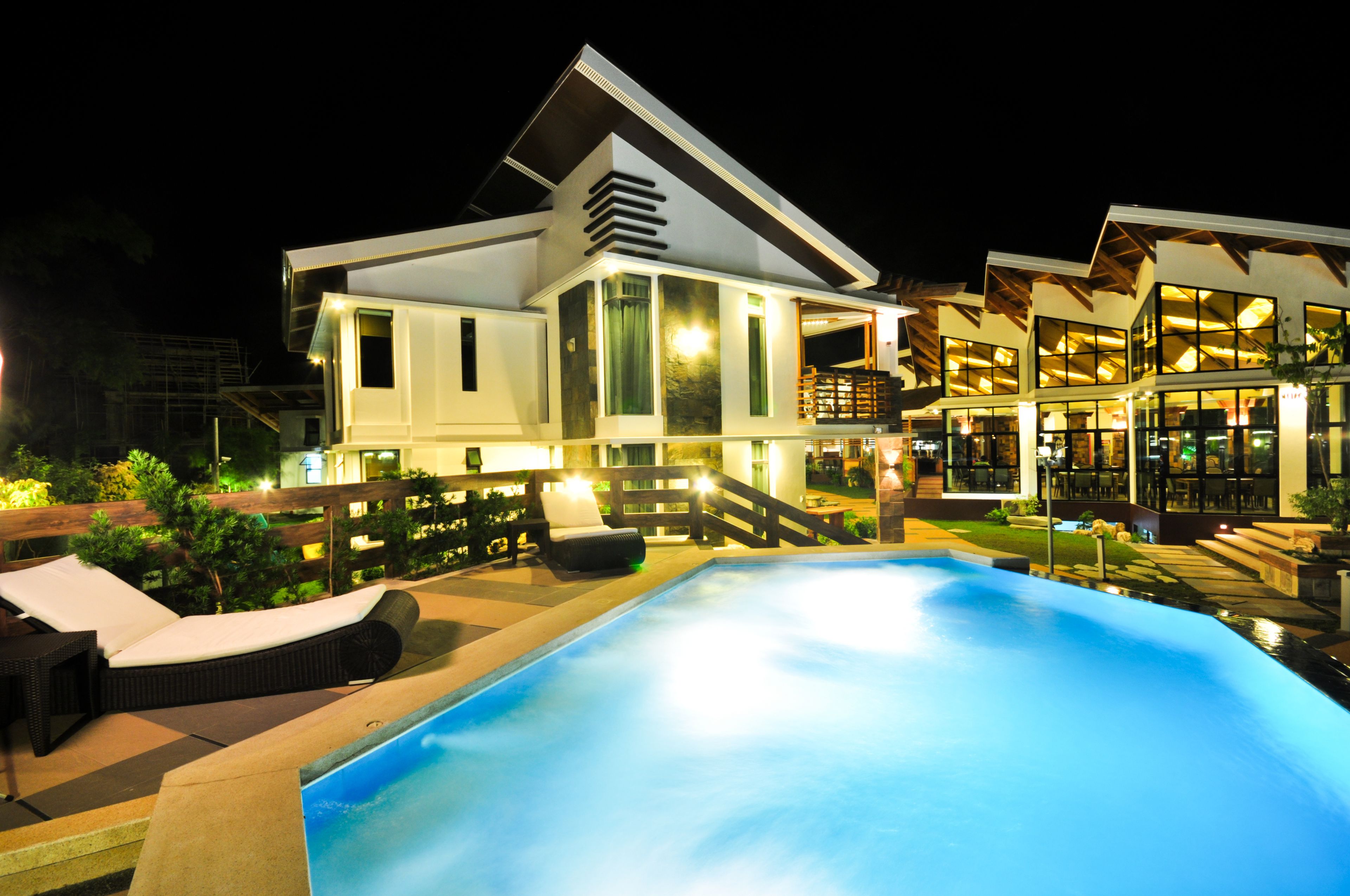 A modern house with a swimming pool, outdoor seating, and a well-lit patio area.