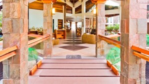 A grand staircase with stone pillars and wooden railings leading to a high ceiling with exposed beams.
