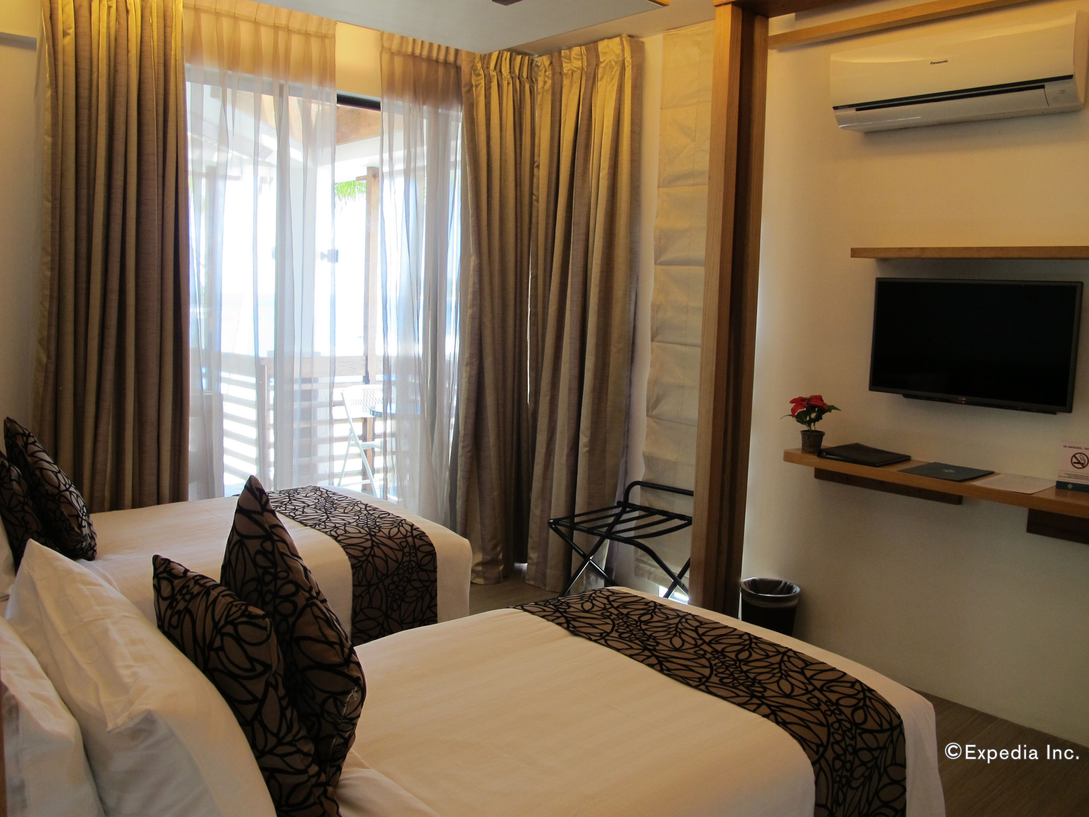 A hotel room with two beds, a TV, a small table with a plant, and a window with curtains.