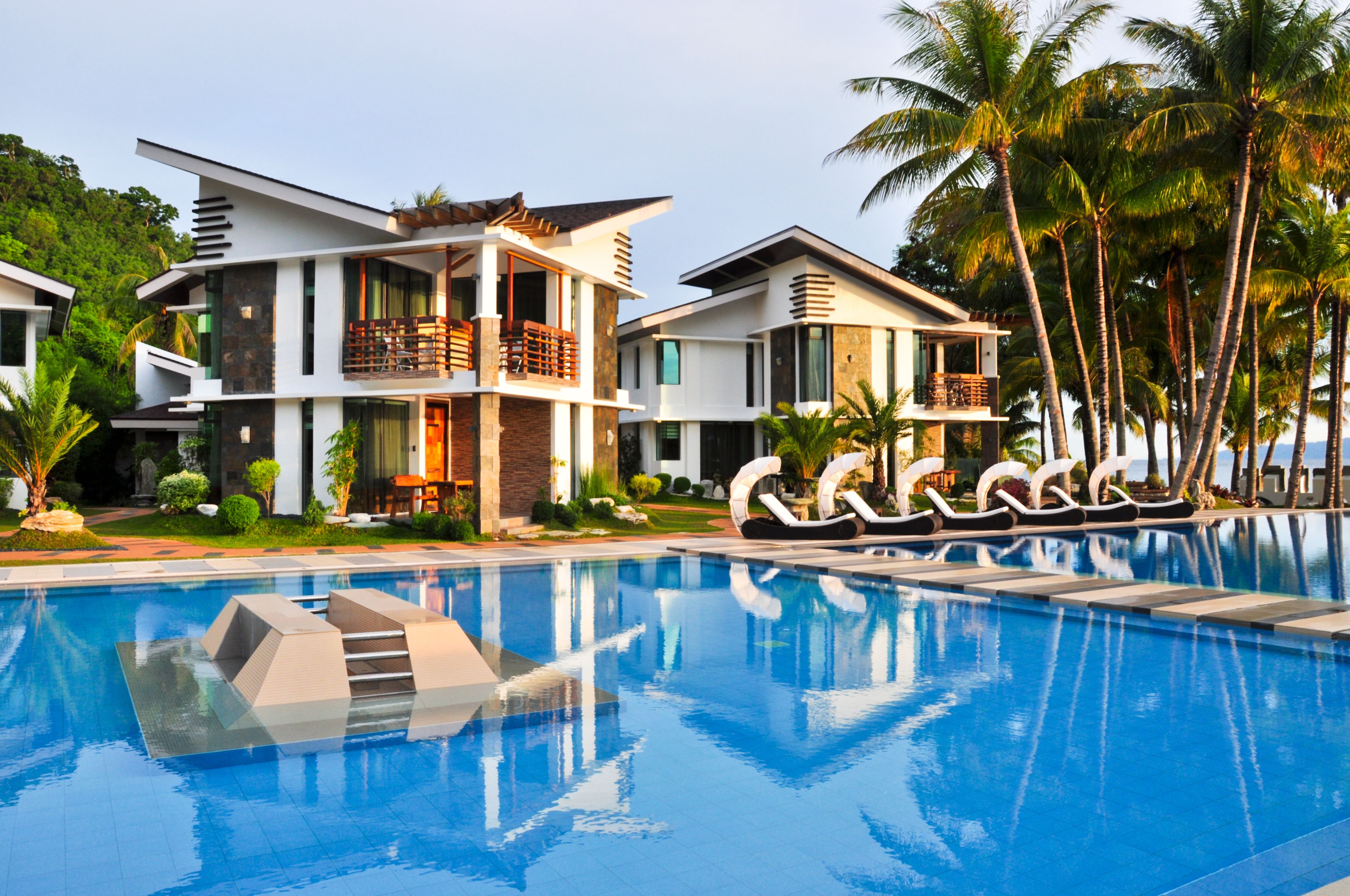 A modern resort with a swimming pool, multiple-story buildings, and palm trees.