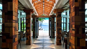 A corridor with wooden beams and a patterned floor, leading to a beach view.