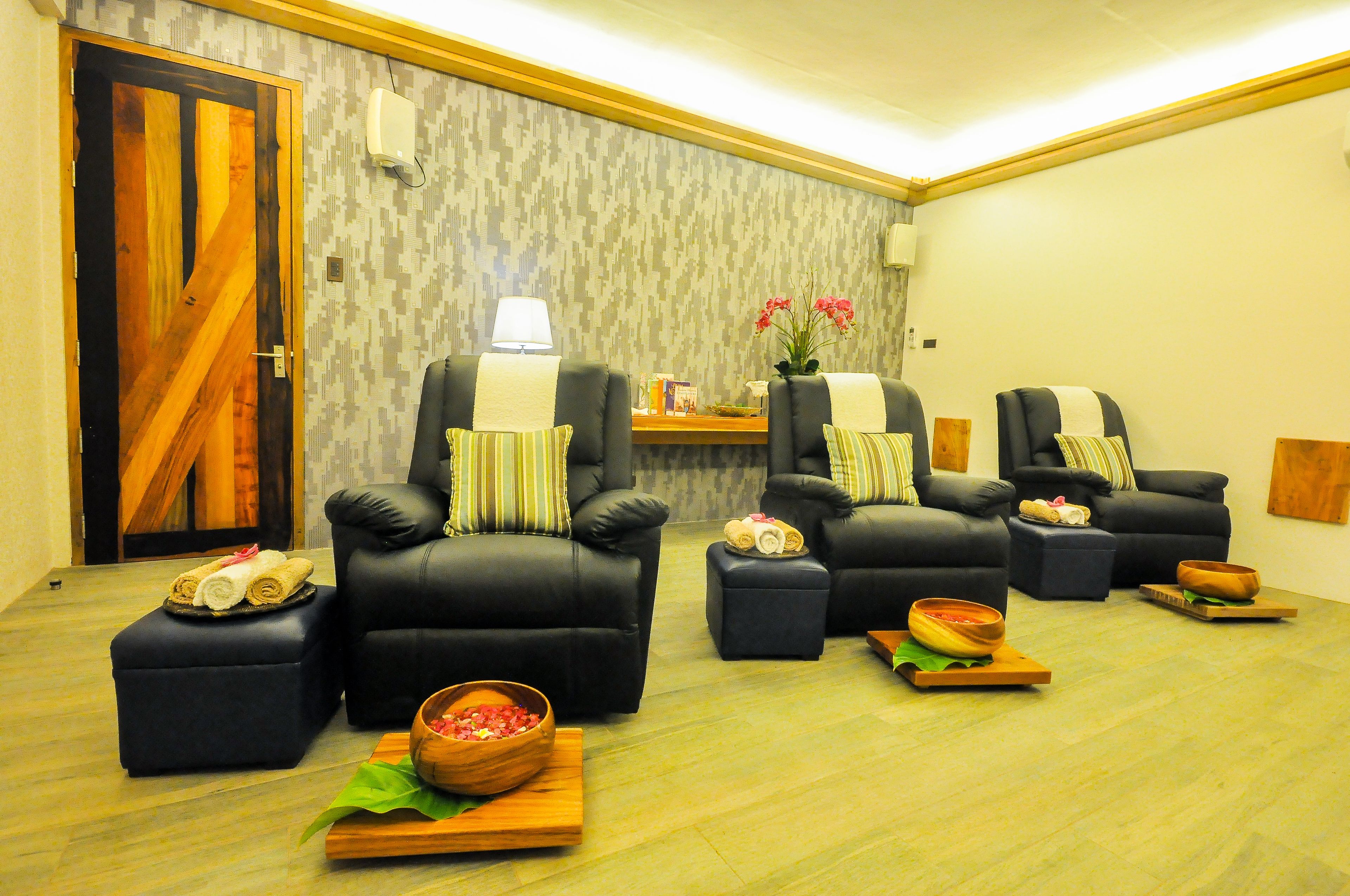 A room with four black leather chairs, each with a pillow and a small table with a bowl and a rolled towel.