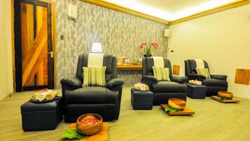 A room with four black leather chairs, each with a pillow and a small table with a bowl and a rolled towel.