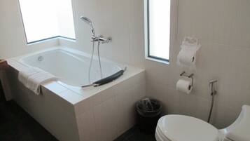 A modern bathroom with a bathtub, toilet, and a window providing natural light.