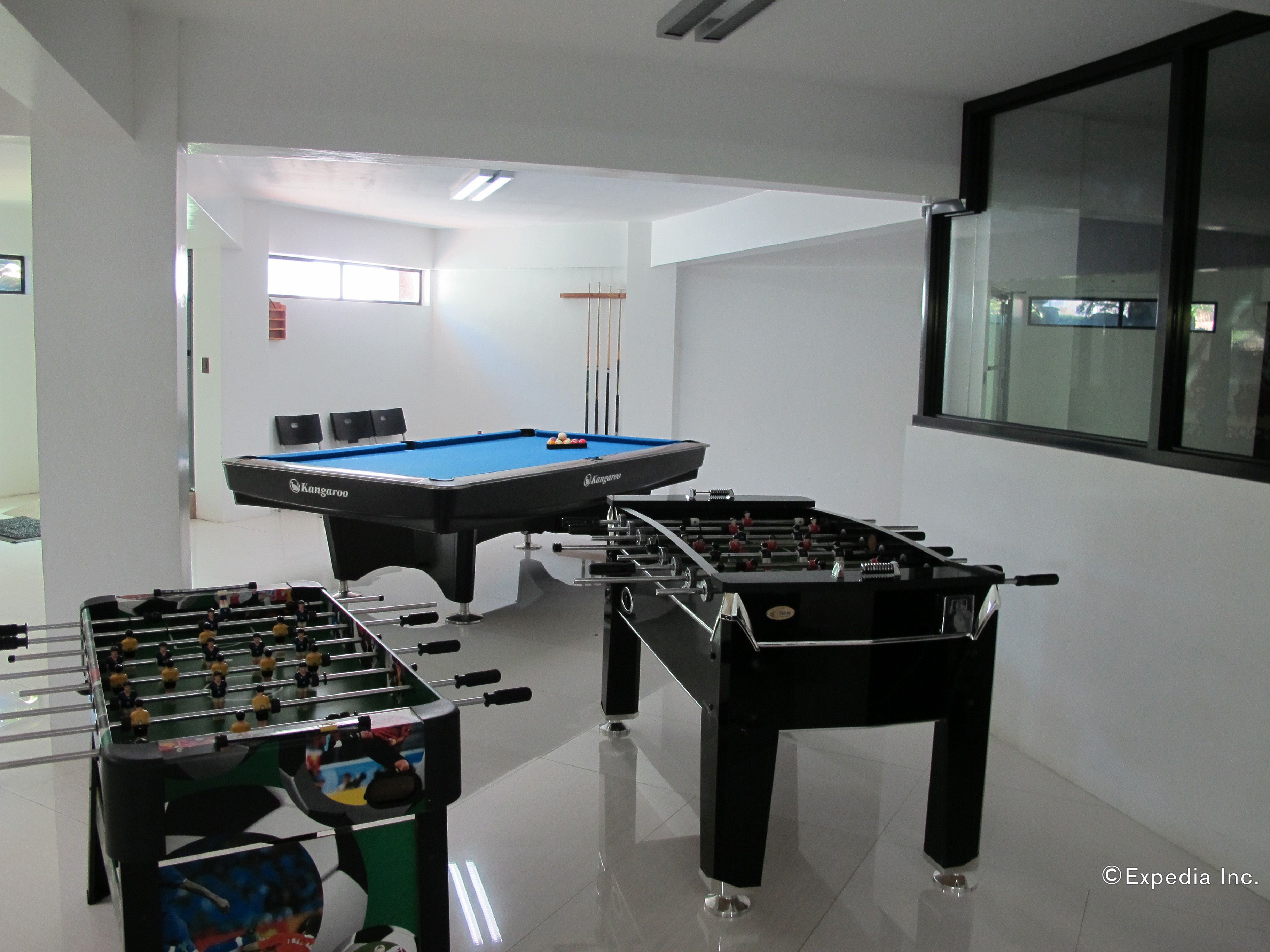 A room with a pool table, two foosball tables, and a window with blinds.