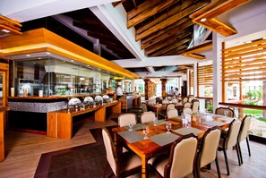 A modern restaurant with a central bar, dining tables with chairs, and a view of the outdoors. - Infinity Resort (Puerto Galera)