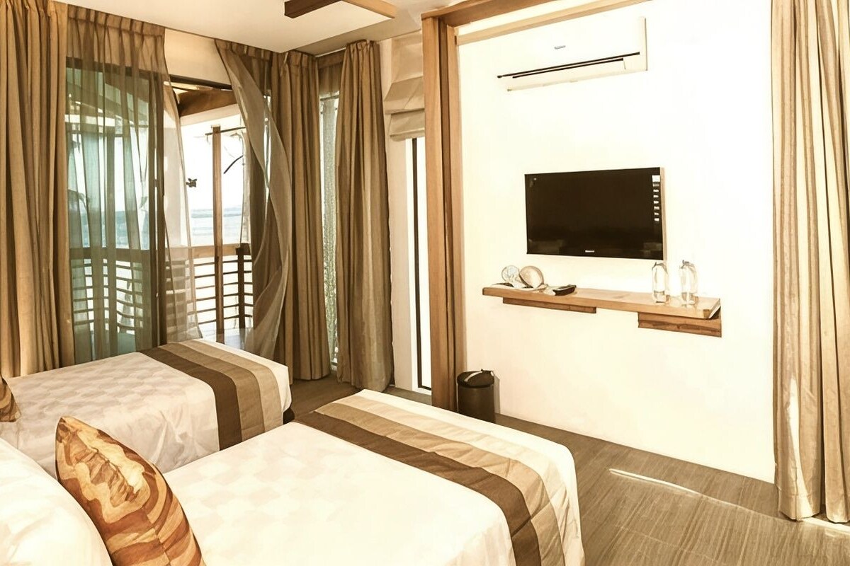 Quarto de hotel com duas camas, televisão e janela com cortinas.