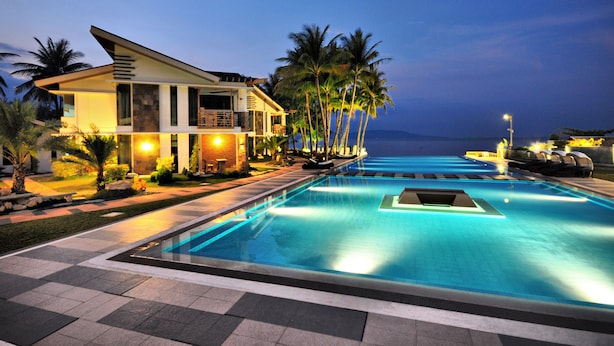 A modern hotel with a swimming pool, palm trees, and a view of the ocean at dusk.