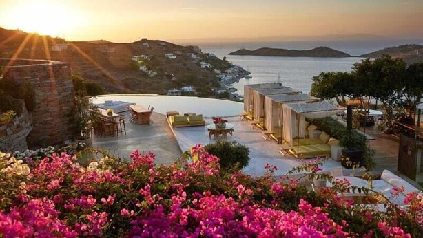 A terrace with outdoor seating, a view of the sea, and a sunset. - Aigis Suites (Kea)