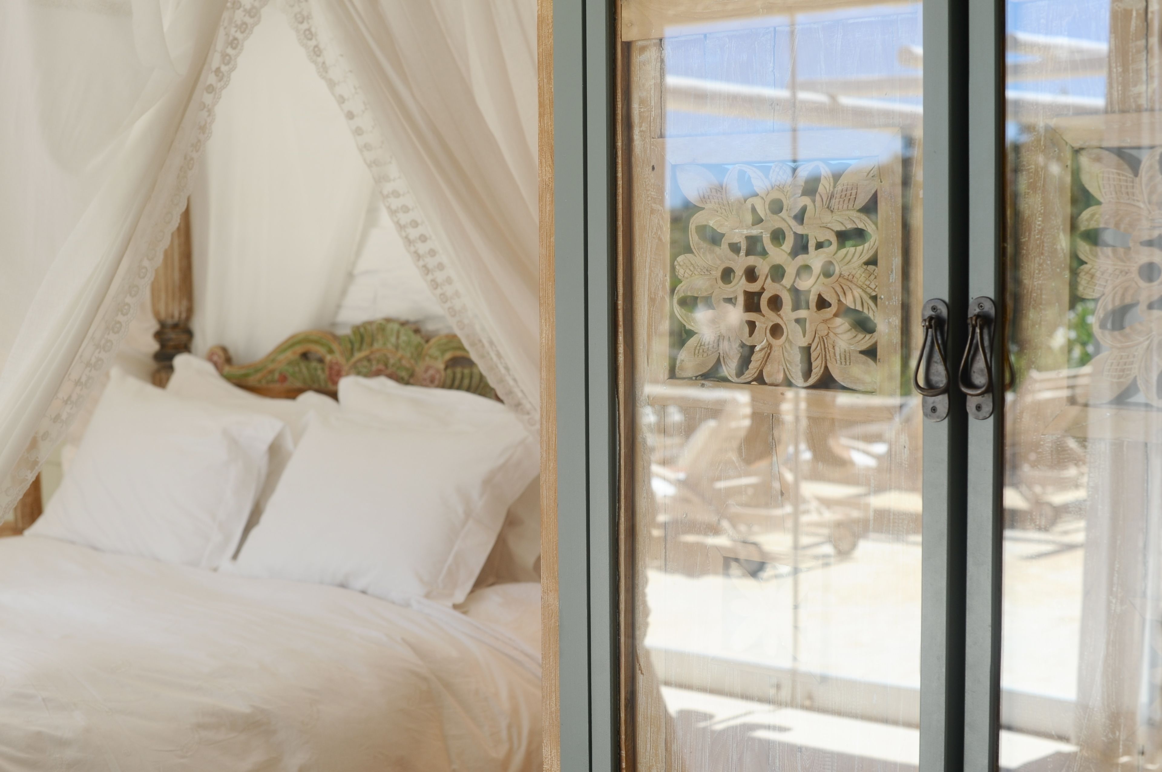 Ein Schlafzimmer mit Baldachinbett, Glastür mit Dekoration und Blick auf Gartenmöbel.