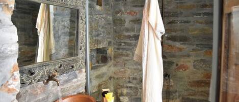 A bathroom with a stone wall, a copper sink, a mirror, and a towel hanging on the wall.
