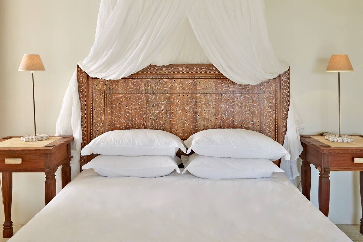 Un dormitorio con cama a dosel, dos mesitas de noche con lámparas y un cabecero decorativo.