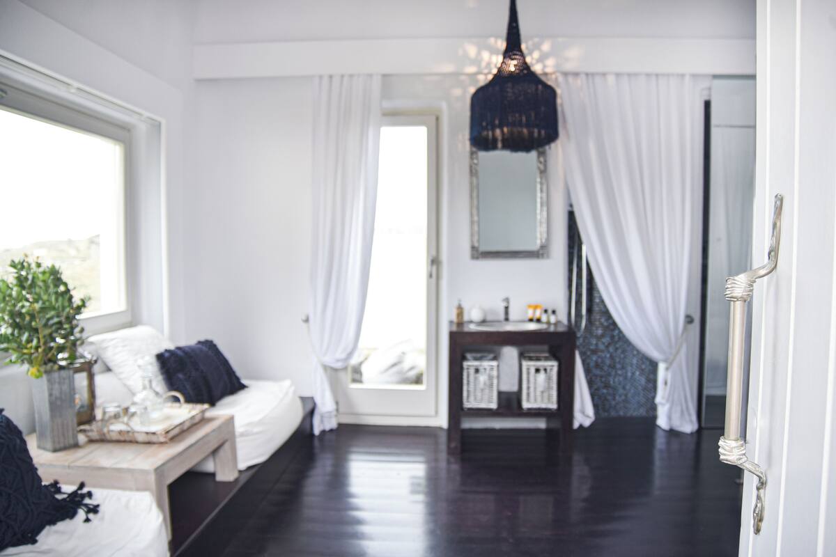 Una habitación con una cama, una mesita de noche con una bandeja, una lámpara colgante, un espejo y una puerta con pomo.