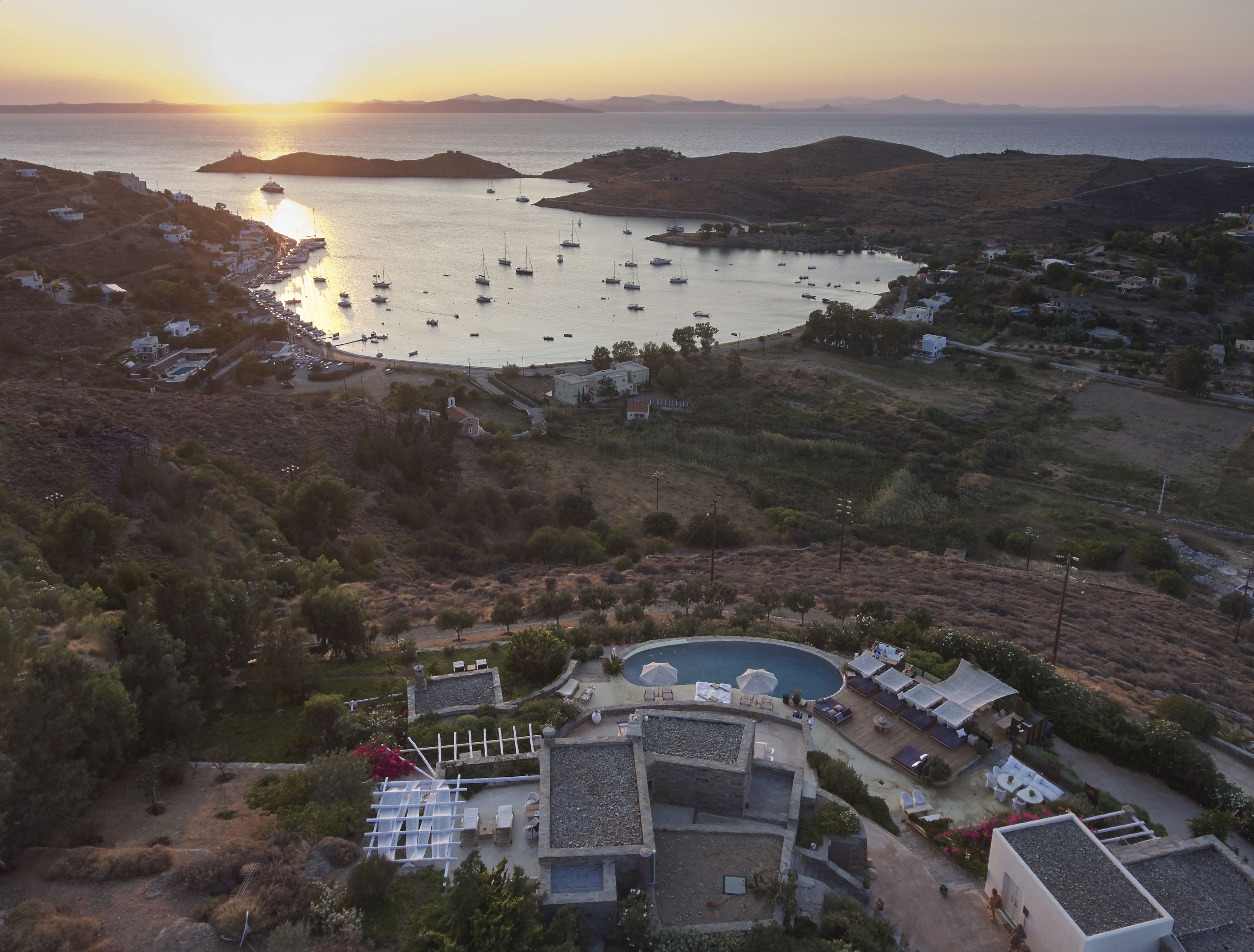 A coastal property with a swimming pool, outdoor seating, and a view of the sea and boats.