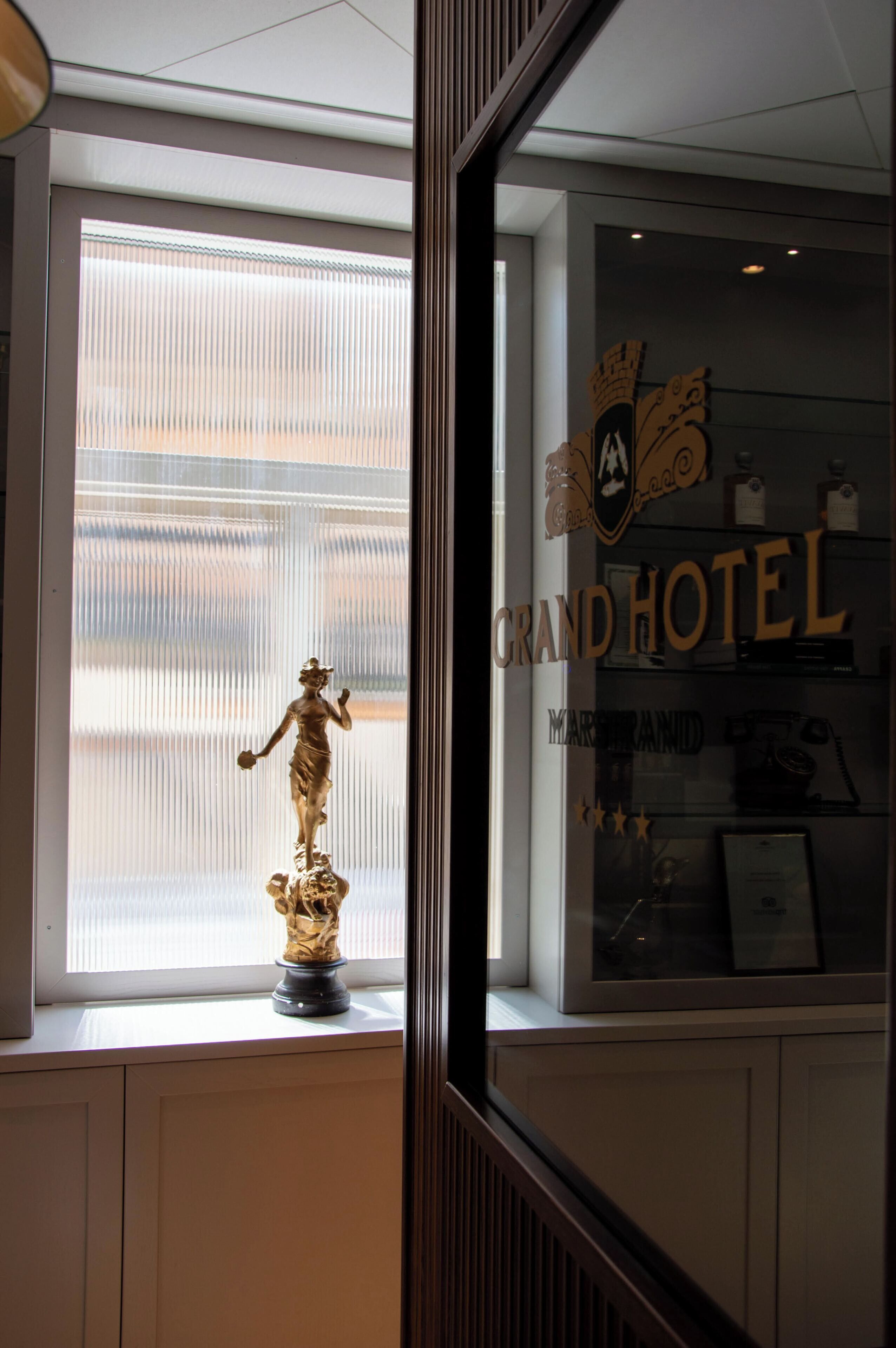 Ett fönster med en staty, en skylt med texten ”Grand Hotel” och en inramad tavla på fönsterbrädan.