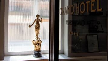 Ett fönster med en staty, en skylt med texten ”Grand Hotel” och en inramad tavla på fönsterbrädan.